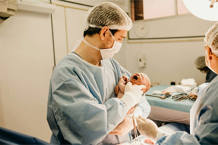 Doctor in surgical attire holding newborn in delivery room, illustrating common health myths discussed by doctors.