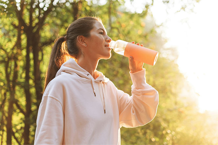 Young woman drinking water outdoors, highlighting common health myths discussed by doctors on wellness and hydration.