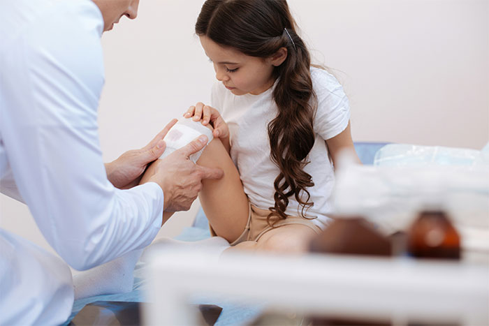 Doctor examining a young girl's injured knee, demonstrating care while addressing common health myths in a clinical setting.