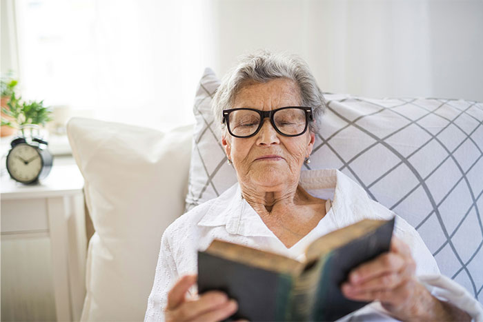 Elderly woman wearing glasses reading a book in bed, highlighting doctors exposing health myths and facts.