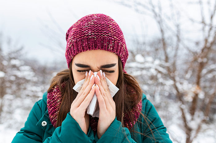 Woman in winter clothes sneezing into a tissue outdoors, illustrating common medical myths doctors are shocked people believe.