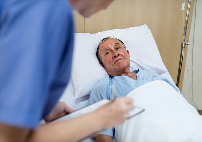 Elderly man in hospital bed looking skeptical at nurse taking notes, illustrating faking illnesses concept.