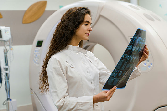 Female doctor examining brain scans near MRI machine, highlighting cases of people faking illnesses and getting exposed.
