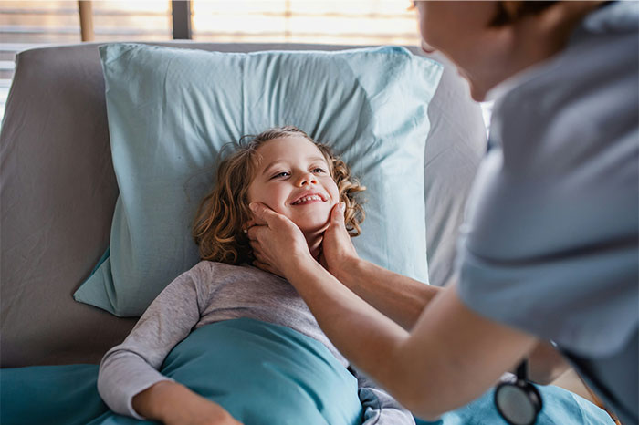 Young child lying in bed smiling while a nurse gently checks for illness, illustrating faked illness exposure.