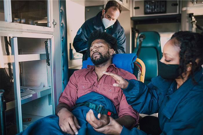 Man appearing to fake illness is attended by emergency medical personnel inside an ambulance during a medical call.