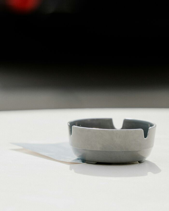 Gray ashtray on a white surface with a blurred dark background, highlighting a simple and minimalistic setting.
