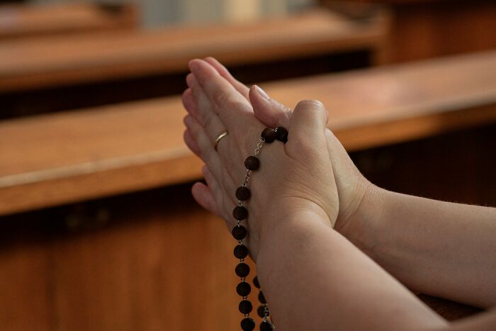 Hands holding a rosary in a wooden pew, representing patience and challenges faced by tattoo artists with difficult clients.