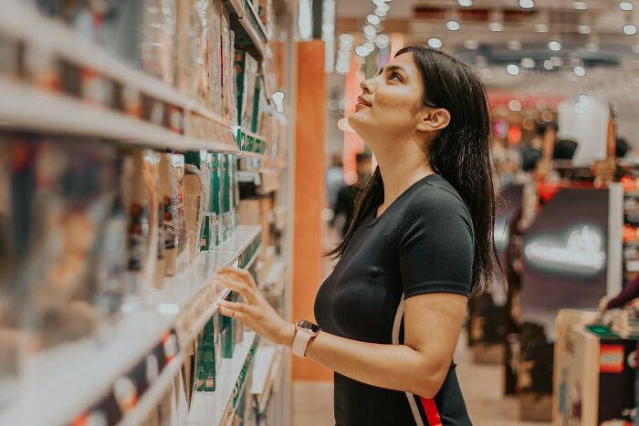 Woman browsing items on supermarket shelves, exploring unhinged money-saving tips that people swear actually work.