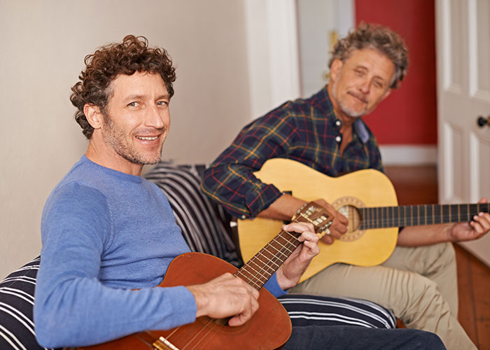 Two men playing acoustic guitars indoors, illustrating people who tried living double lives.