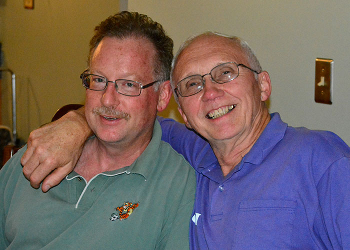 Two men wearing glasses smile and pose together in a casual setting, illustrating stories of people living double lives.