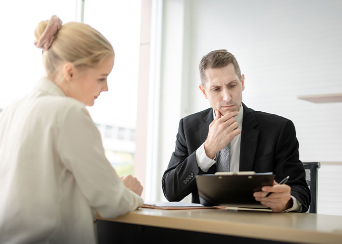 Man in suit thoughtfully reviewing documents with woman at office desk, illustrating people living double lives concept.