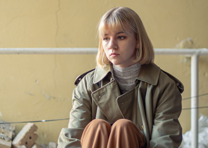 Young woman in a trench coat sitting alone, reflecting on times people tried living double lives to fool others.