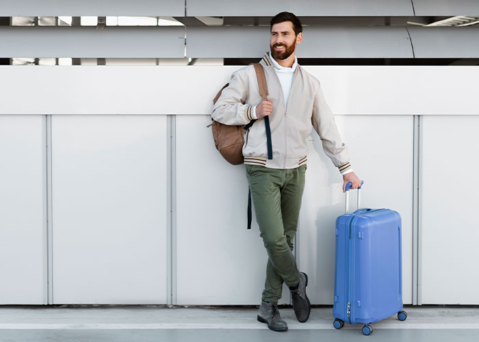 Man with backpack and suitcase standing against a wall, representing people living double lives trying to fool others.