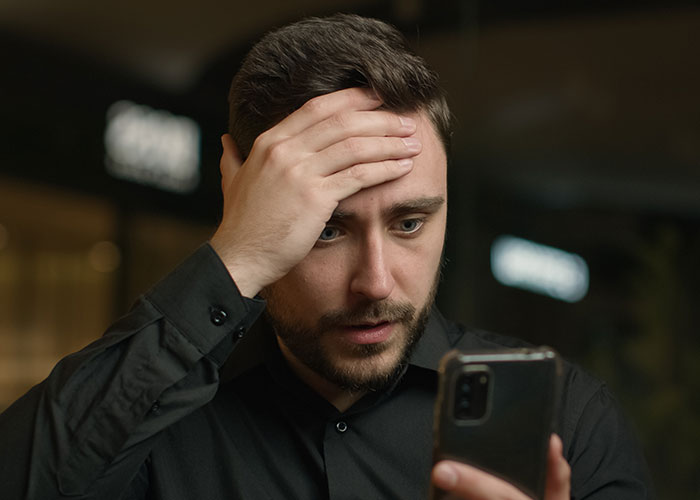 Man in black shirt looking shocked at phone, illustrating people who tried living double lives and fooling others.