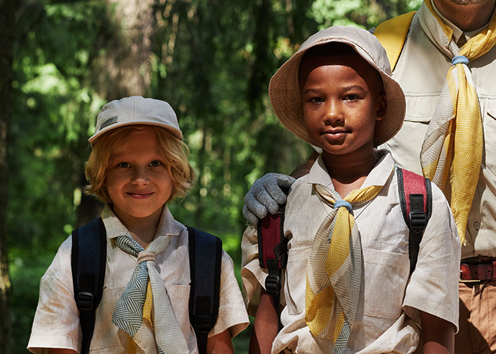 Two boys wearing scout uniforms and backpacks outdoors, representing themes of people living double lives.