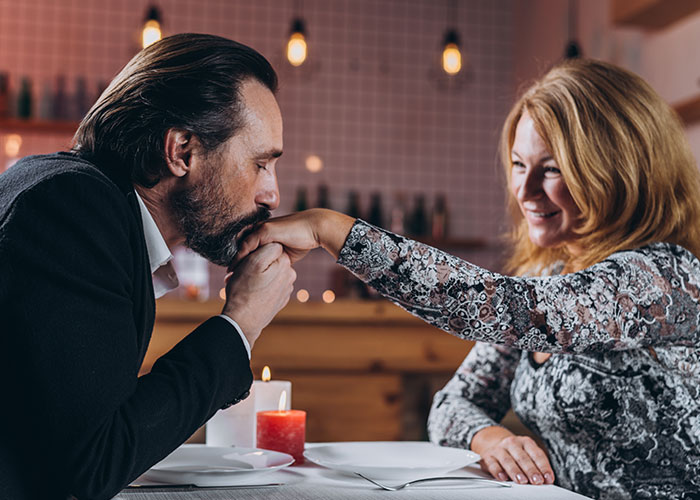 Man kissing woman’s hand on a romantic dinner date, illustrating moments from people living double lives and trying to fool others.