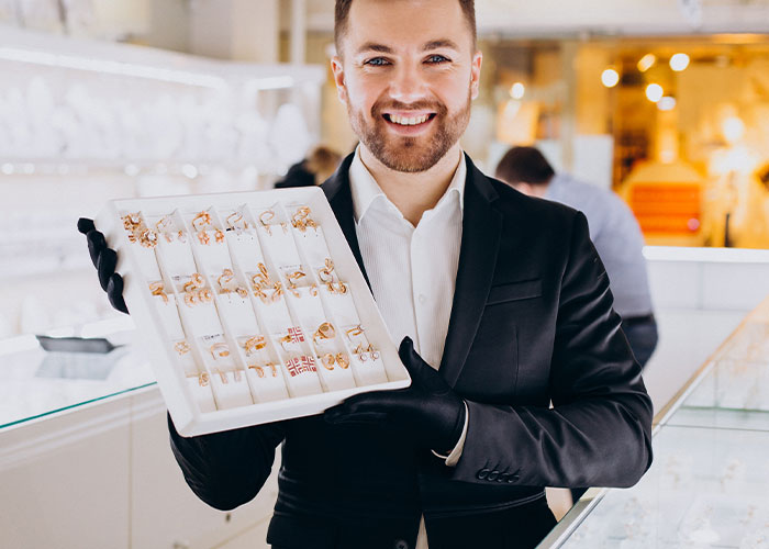 Man in a suit wearing black gloves holds a tray of jewelry, illustrating the concept of people living double lives.