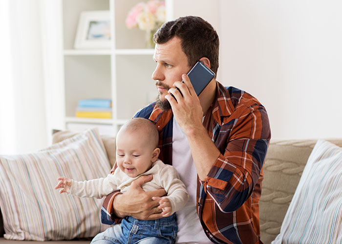 Man holding a baby and talking on the phone, illustrating the concept of people living double lives attempting to fool others.