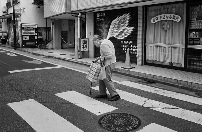 Elderly person crossing a street using a cane, captured in a powerful street photo showcasing the beauty and wisdom of old age.