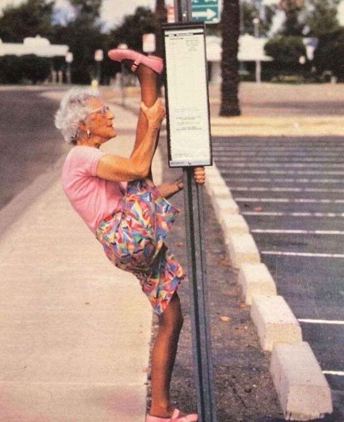 Elderly woman stretching her leg on a street signpole, showcasing the beauty and wisdom of old age.