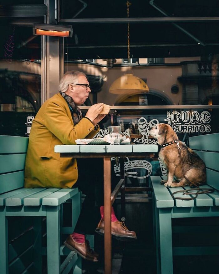 Elderly man in a mustard jacket sharing a meal with his dog at a street cafe, capturing beauty and wisdom of old age.