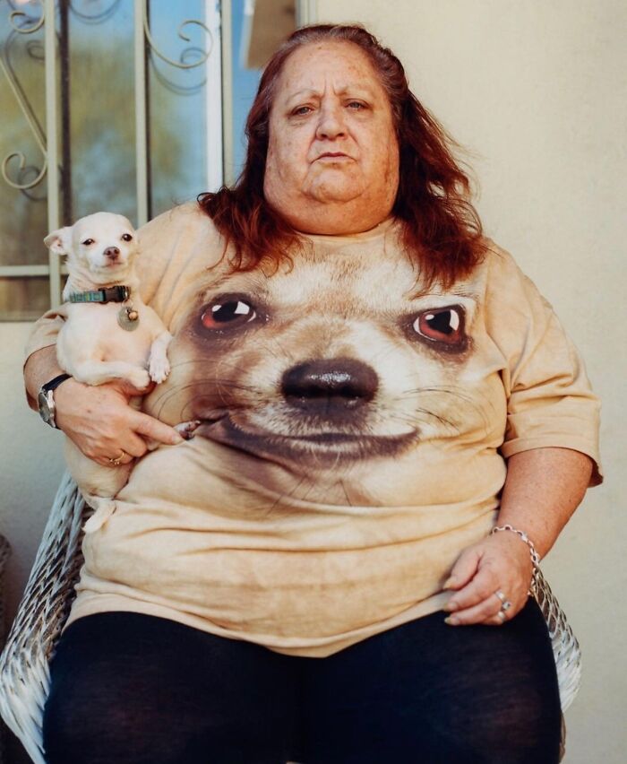 Older woman holding a small dog, wearing a shirt with a large dog face, capturing beauty and wisdom of old age in street photography.