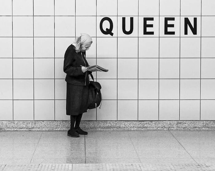 Elderly woman reading a book in a street setting, capturing the beauty and wisdom of old age in black and white.