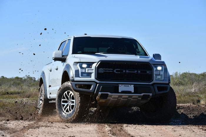 White Ford truck driving off-road on a dirt path with mud splashing, representing dream truck loan inheritance concepts.