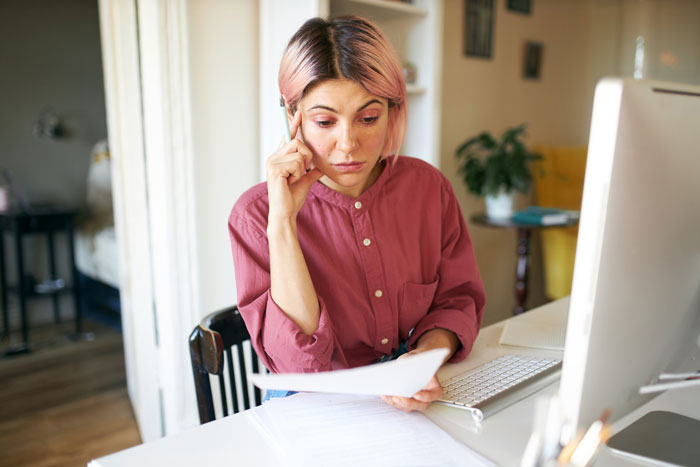 Woman with pink hair looking worried while reviewing documents at desk with computer, related to dream truck loan inheritance