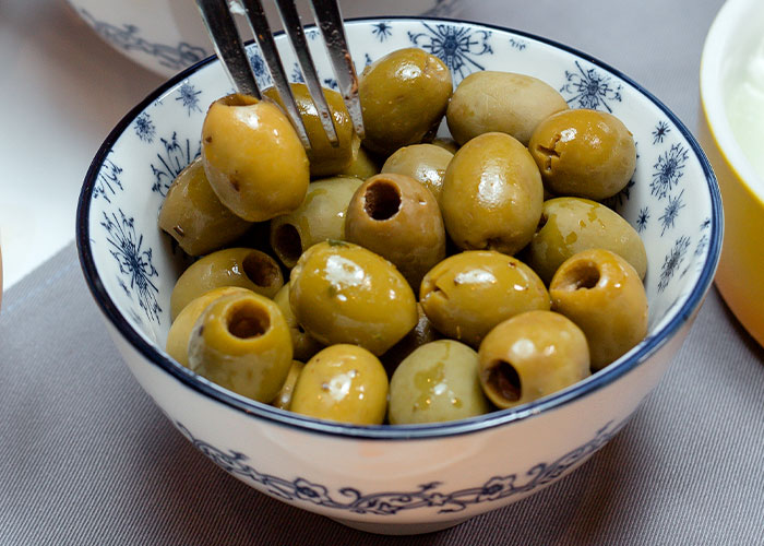 Bowl of green olives being picked up with a fork, illustrating food industry workers and customer experiences.