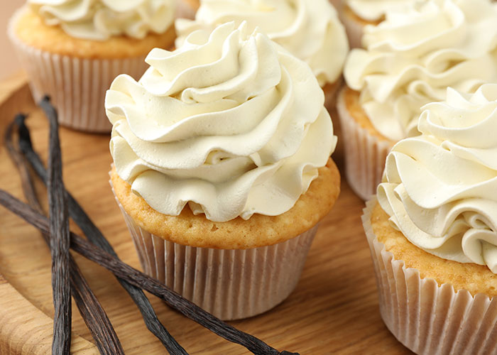 Vanilla cupcakes with creamy frosting displayed on a wooden board with vanilla pods, highlighting food industry customers.