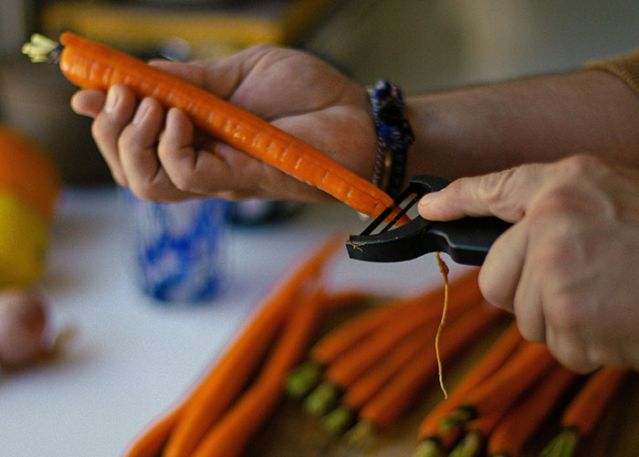 Person peeling a carrot with a peeler in a kitchen, illustrating food industry workers and dumbest customers.