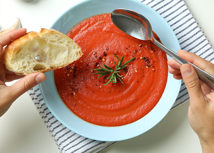 Hands holding bread and spoon over a bowl of tomato soup, illustrating food industry workers’ dumbest customers stories.