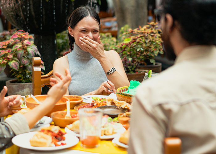 A woman laughing with friends at a restaurant table filled with various dishes, illustrating food industry customer moments.