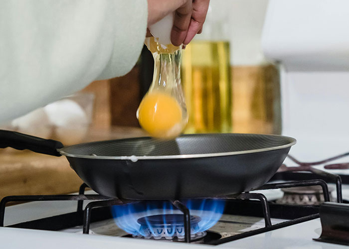 Person cracking an egg into a frying pan over a stove flame, related to food industry workers and dumb customers.