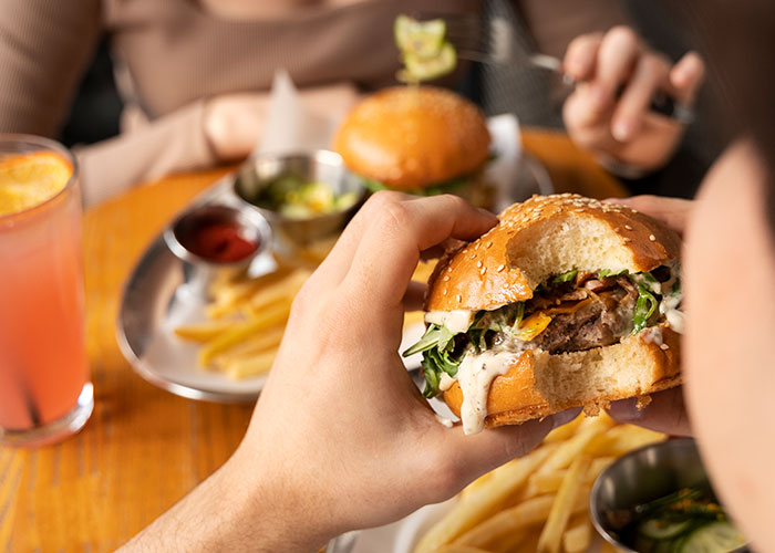 Person holding a partially eaten burger with fries and drinks on a table, food industry workers’ memorable customers.