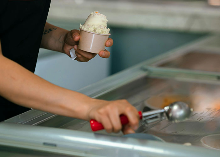 Person scooping ice cream with red-handled scooper, highlighting food industry workers and dumbest customers.