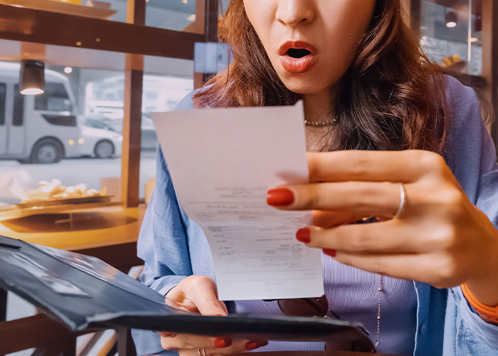Customer in a restaurant looking shocked while reading a bill, illustrating dumbest customers in the food industry.