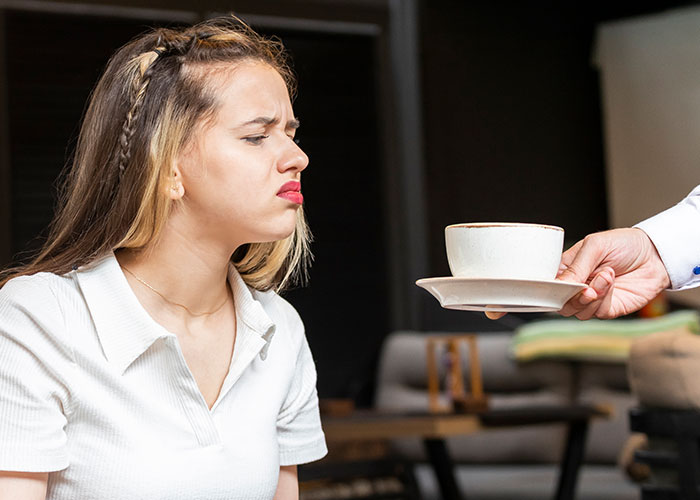 Young woman making a disgusted face as a waiter offers a cup of coffee, illustrating dumbest customers in food industry stories.