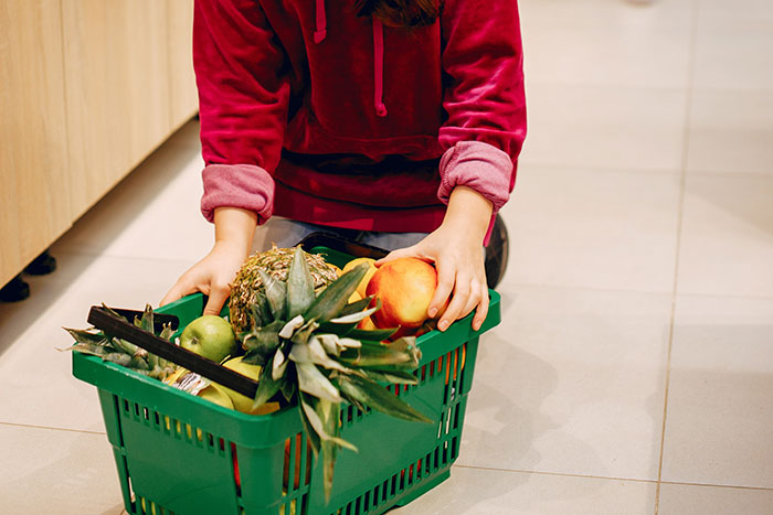 Person holding a green basket filled with groceries illustrating unhinged ways company credit cards were used