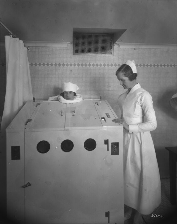 Nurse operating an old medical device with patient’s head exposed, showcasing old-school medical equipment in a clinical setting.