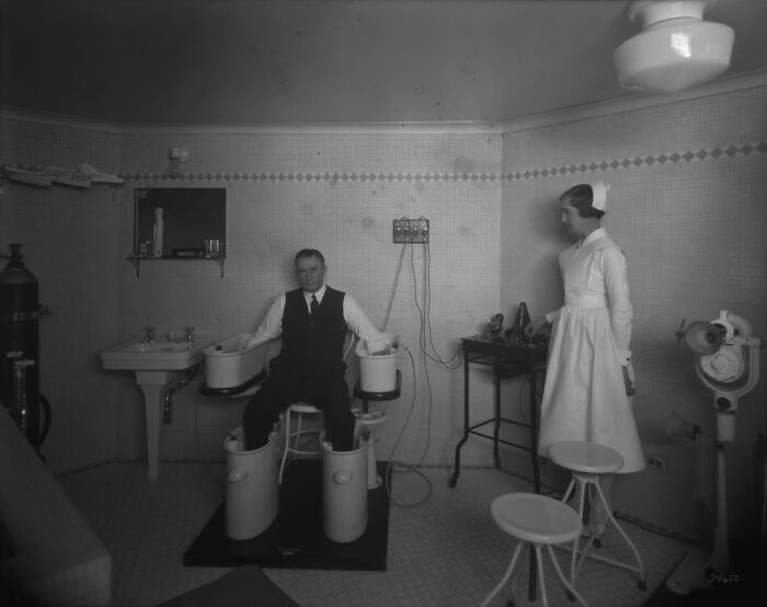 Black and white old-school medical pic showing a patient undergoing electrotherapy with a nurse assisting in a vintage clinic.