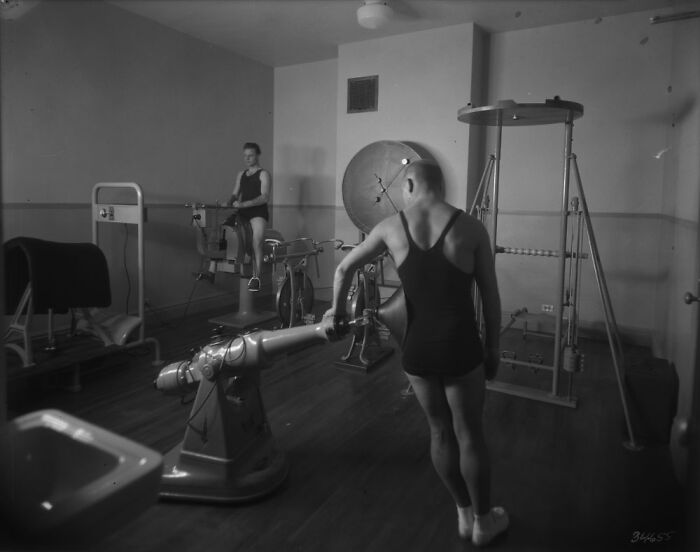 Black and white image of old-school medical equipment with patients using rehabilitation machines in a vintage clinic setting.