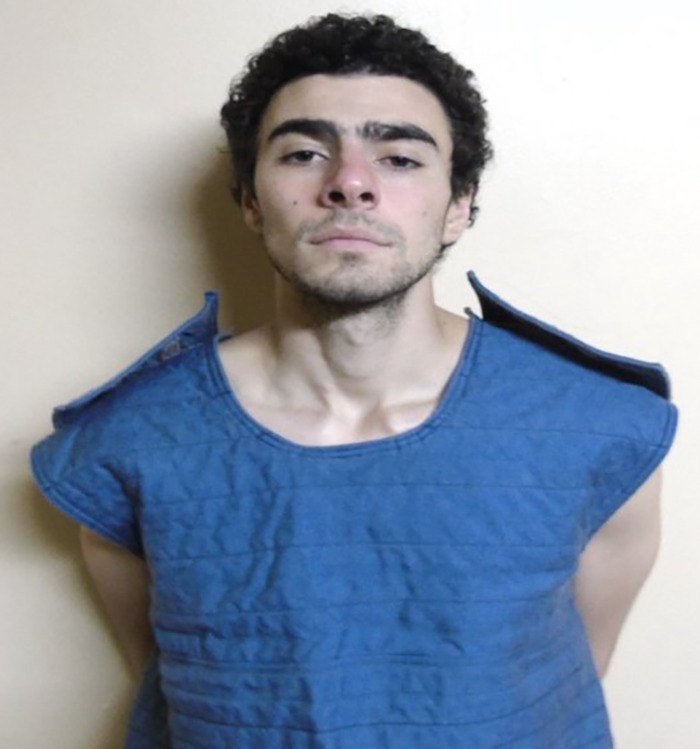 Tyler Robinson wearing a blue padded vest, standing against a plain wall as Charlie Kirk suspect appears in court.