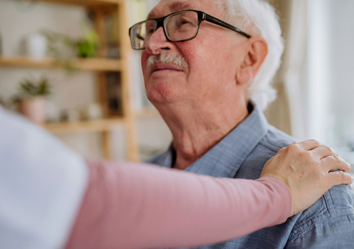 Elderly man with glasses being comforted by a person, illustrating a couple confronted by neighbor over affair claims.