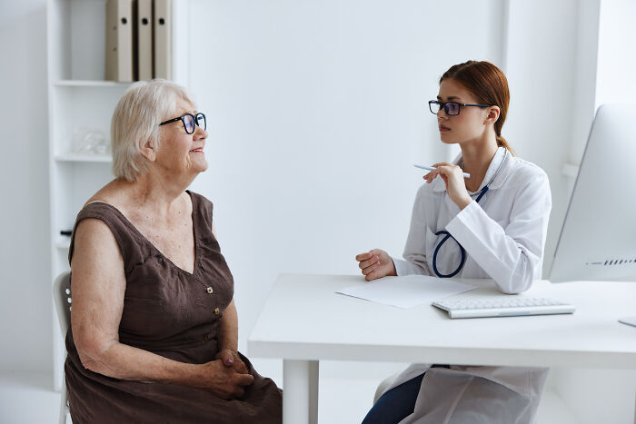 Young female doctor with stethoscope listening to elderly patient in a medical office discussing health concerns.