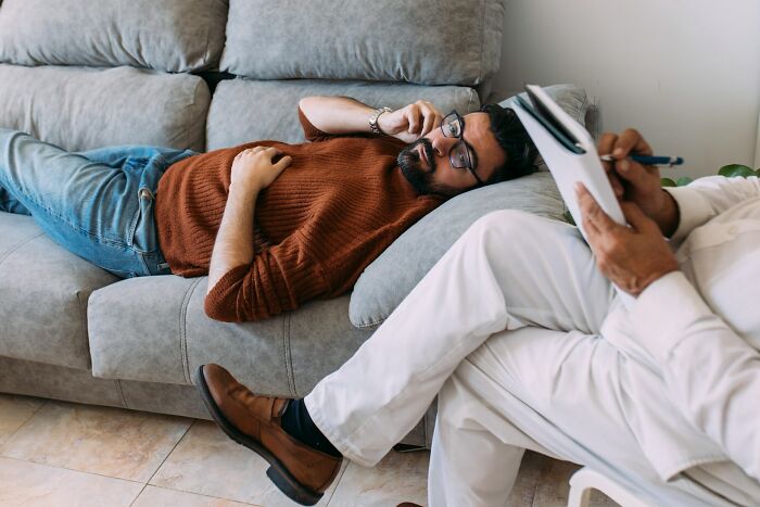 Man in happy marriage lying on couch talking on phone during therapy session with counselor taking notes nearby