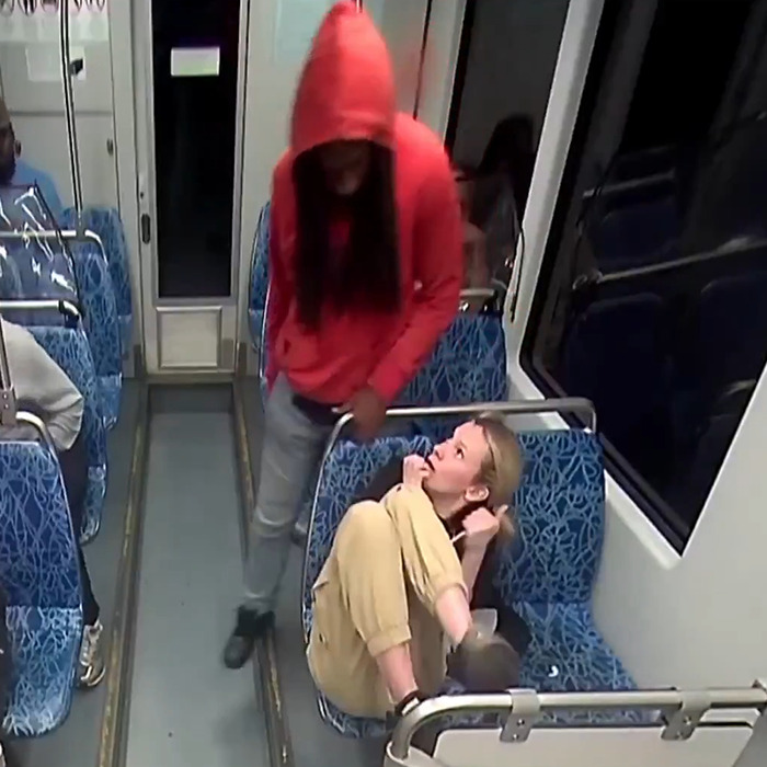 Person in red hoodie standing near seated woman on public transit, with Elon Musk and Andrew Tate mural donation theme. Person in red hoodie standing near seated woman on public transit, with Elon Musk and Andrew Tate mural donation theme.