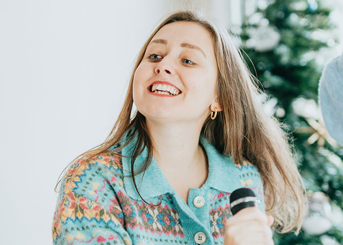 Young woman smiling and speaking into a microphone during a casual moment about facepalm-worthy doctor’s visits.