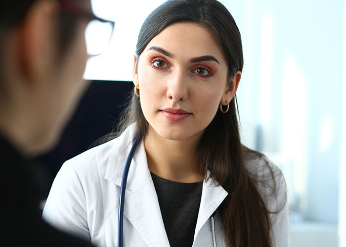 Young female doctor attentively listening to patient during a facepalm-worthy doctor’s visit in a clinical setting
